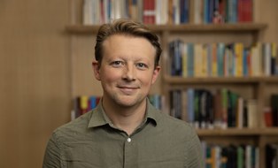 blonder Mann vor einer Bibliothek