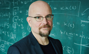 Foto von Prof. Dirk Brockmann vor einer Tafel mit Formeln.