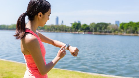 Foto von einer jungen Frau an einem Fluss, die ihre Smart Watch fürs Lauftraining startet