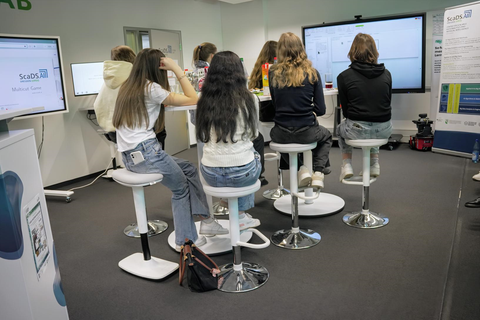Foto. Sieben Mädchen sitzen rings um einen Tisch im Living Lab.