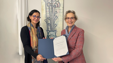 A photo of two women, smiling and holding a blue folder with a white certificate inside.