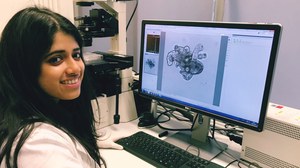 A woman using a microscope, the object under the microscope can be seen on a connected monitor