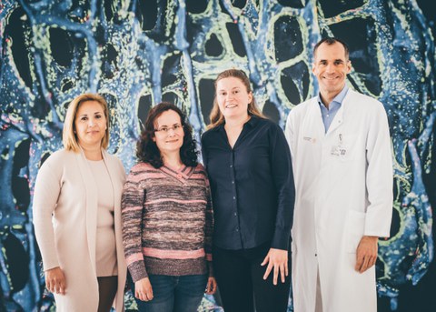 four people standing and smiling in front of a colorful background