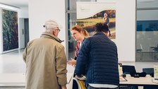 The speaker from feelSpace GmbH at their Information stand talking to a group of elderly people .