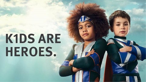 Ein Poster. Auf der linken Seite ist ein großer Text "K1DS ARE HEROES" zu sehen. Auf der rechten Seite des Bildes stehen zwei Kinder, die als Superhelden gekleidet sind, nebeneinander.