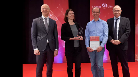 four people standing next to each other smiling. A women is holding a statuette and a man is holding a certificate. 