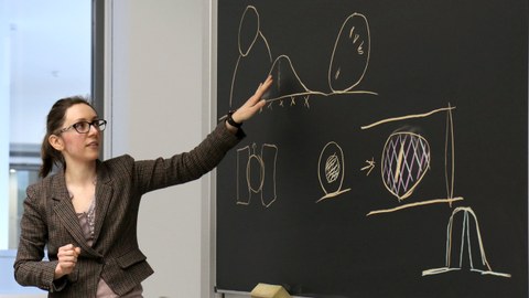 Woman standing in front of a blackboard with several sketches drawn with chalk