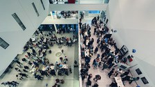 A top down photo of a hall with several floors, filled with visitors and exhibition booths.