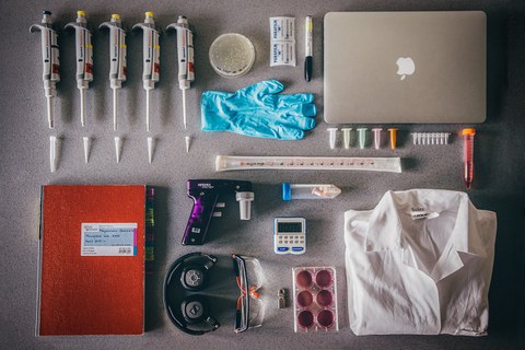 On the poto you can see lab equipment. In the right top corner there is laptop, below it white coat, pipettes and a laboratory notebook 