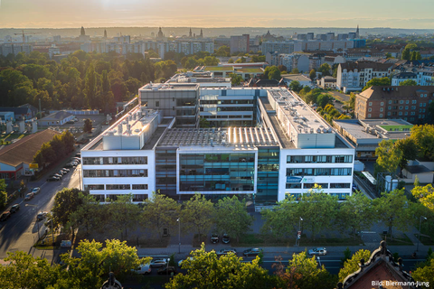 CRTD-Gebäude von einer Drohne aus gesehen. Ein weißes Gebäude mit einer Glasfront, umgeben von Bäumen und einem Dresdner Stadtpanorama.