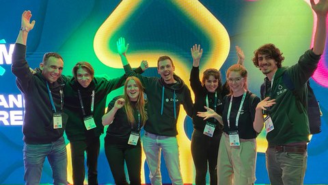 Ein Gruppenbild. 7 Personen die glücklich vor einer digitalen Leinwand posieren.