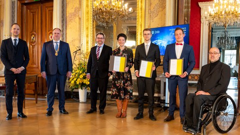 sechs Personen in Anzügen posieren zu einem Foto in einem goldenen Raum