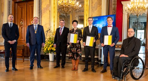 sechs Personen in Anzügen posieren zu einem Foto in einem goldenen Raum