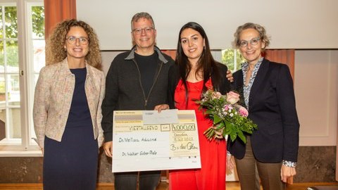 ein Gruppenfoto. Für die Menschen posieren drei Damen und ein Herr. Die jüngste Dame hält Blumen und einen großen Scheck