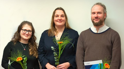 Lächelnde Menschen posieren für ein Gruppenfoto mit Blumen und Urkunden.