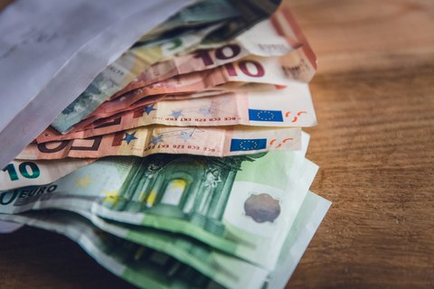 A photo. Euro banknotes lay on the table, partially taken out of a white envelope.