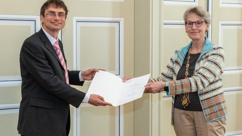 Ein Mann auf der linken Seite erhält ein Diplom von der Frau auf der rechten Seite. Beide lächeln