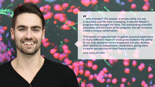 A portrait photo with text. A smiling person on a black background with clustered specks in pink, purple, and green. On the right side of the photo, there is a white rectangle with a big quotation mark and text: ”Why Dresden? The answer is simple: while the city is beautiful and life here is amazing, it was the Master’s program that brought me here. The outstanding scientific education and the heart of the program, the lab rotations, create a unique combination. This wealth of opportunities to gather practical experience in many different research areas gives students the ability to not only appeal to future employers but also develop their abilities as independent researchers, giving them a clearer perspective on their future careers. David, Austria, 2017-2019.”
