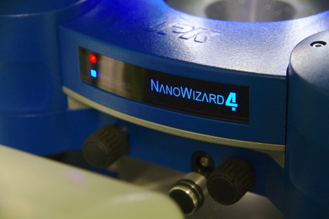 A photo. The background is a metallic blue circle. At the center is a black display with bright blue text reading "NANOWIZARD 4". To the left, there is a red and a blue light.