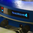 A photo. The background is a metallic blue circle. At the center is a black display with bright blue text reading "NANOWIZARD 4". To the left, there is a red and a blue light.