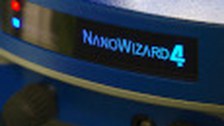 A photo. The background is a metallic blue circle. At the center is a black display with bright blue text reading "NANOWIZARD 4". To the left, there is a red and a blue light.