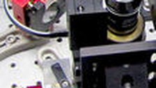 A photo. The image shows a close-up of scientific equipment made of plastic on a metallic surface with small holes. There are two red semicircles and a cylindrical black and silver object.