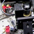 A photo. The image shows a close-up of scientific equipment made of plastic on a metallic surface with small holes. There are two red semicircles and a cylindrical black and silver object.