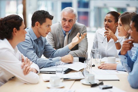 Männer und Frauen, die um einen Besprechungstisch sitzen und miteinander diskutieren