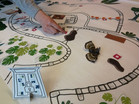 Papier mit darauf gemaltem Spielfeld und Objekte zum Beispiel einer Eingangstür Hand die eine Spielfigur auf dem Feld bewegt