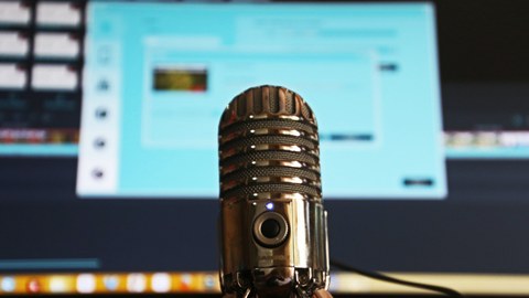 Ein Mikrofon, verschwommen im Hintergrund ein Computerbildschirm