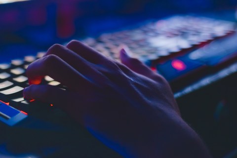 Ein dunkel gehaltenes Foto, darauf eine rot beleuchtete Tastatur mit einer Hand