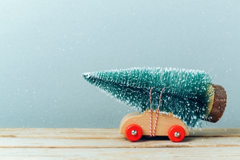 Winterliches Bild mit einem Holzspielzeugauto, welches einen kleinen Holzbaum auf dem Dach gebunden hat