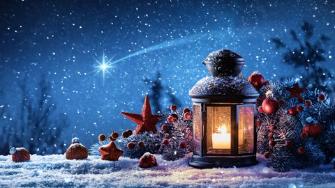 Foto: kleine Laterne auf Schnee, mit Sternenhimmel und Tannenzweig im Hintergrund 