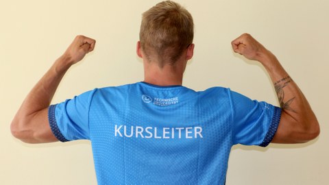 Foto: muskulöser Mann mit blauem T-Shirt, auf dem "Kursleiter" steht