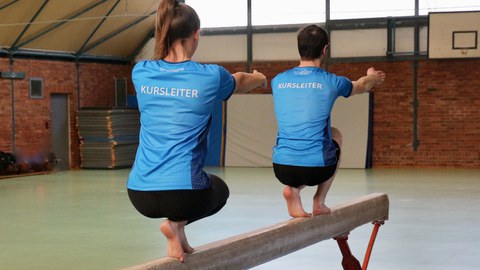 Foto zwei Sportler auf dem Sportbalken in blauen Shirts mit dem Schriftzug "Kursleiter"