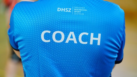 Foto Rückenansicht einer Person im blauen Shirt mit der Aufschrift "Coach"