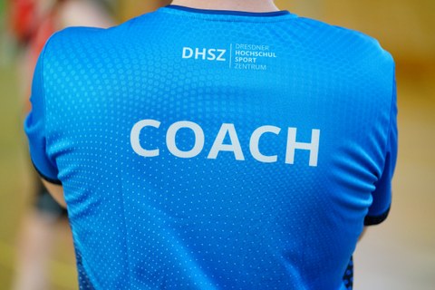 Foto Rückenansicht einer Person im blauen Shirt mit der Aufschrift "Coach"