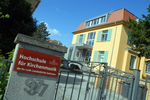 Foto gelb verputze Villa mit schmiedeeisernem Tor, am Torpfosten ein Schild mit der Aufschrift "Hochschule für Kirchenmusik 