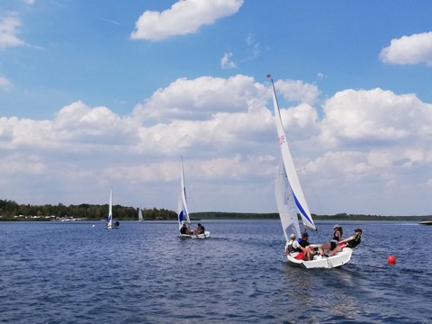 Foto mehrere Segelboote fahren hintereinander über einen See, Himmel mit weißen Wolken im Hintergrund