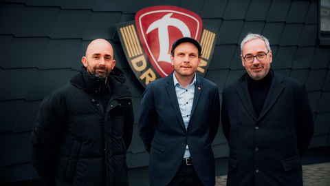 Foto: drei Männer, Marko Schimke, David Fischer und Jan Gerken stehen vor dem Logo von Dynamo Dresden