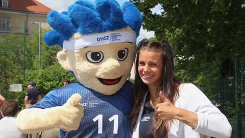 Foto von einer jungen Frau Arm in Arm mit einer Plüschfigur mit blauen Haaren und blauem T-Shirt