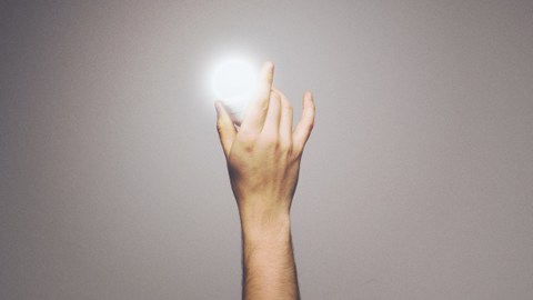 Foto: eine Hand hält eine leuchtende Glühbirne