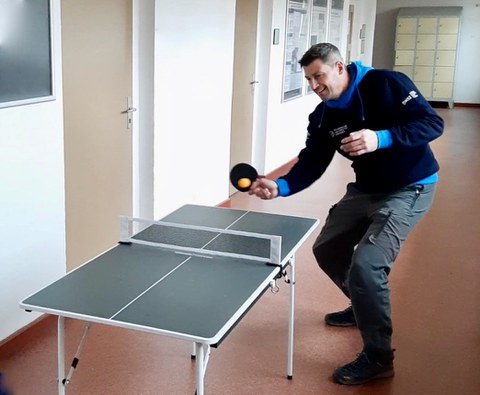 Foto: Mann in blauem Kapuzenpullover spielt an einer Mini-Tischtennisplatte Tischtennis