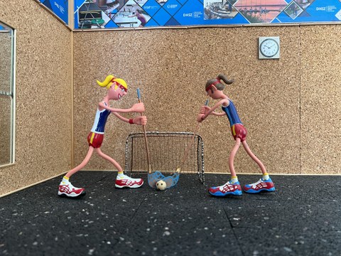 Foto 2 Puppen mit Floorballschlägern in Sporthalle, alles in Miniatur