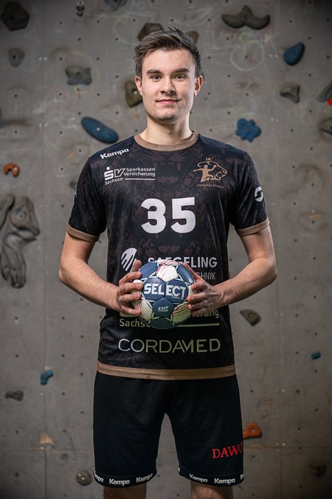 junger Mann im Sportkleidung mit Handball in der Hand steht vor Kletterwand