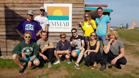 Teilnehmer des USZ Kite Camp 2019 zeigen das Victoryzeichen vor einer Holzhütte