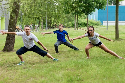 Foto: drei Personen in Taichi-Pose auf einer Wiese