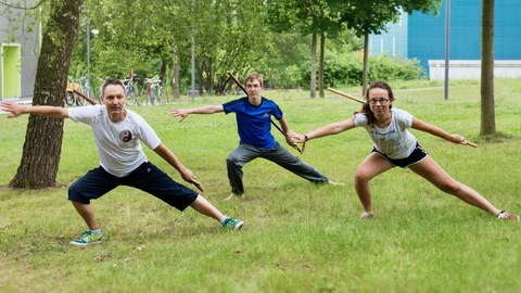 Foto: drei Personen in Taichi-Pose auf einer Wiese