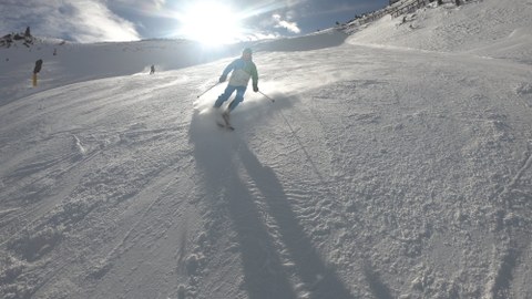 Foto Ein Skifahrer im blau-weißem Skianzug fährt im Gegenlicht mit Parallelschwung einen Hang hinunter