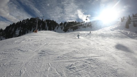 Foto beschneiter Skihang im Gegenlicht mit 2 Skifahrern im Hintergrund